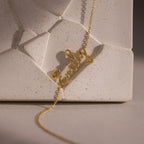 Cursive Name Bracelet in 18K Gold shown resting on a textured, geometric beige surface—a stunning custom jewelry piece that adds a personal touch to any look.