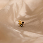 The Onyx Flower Studs, with gold and black onyx in a delicate flower shape, rest on beige satin—perfect dainty earrings for any occasion.