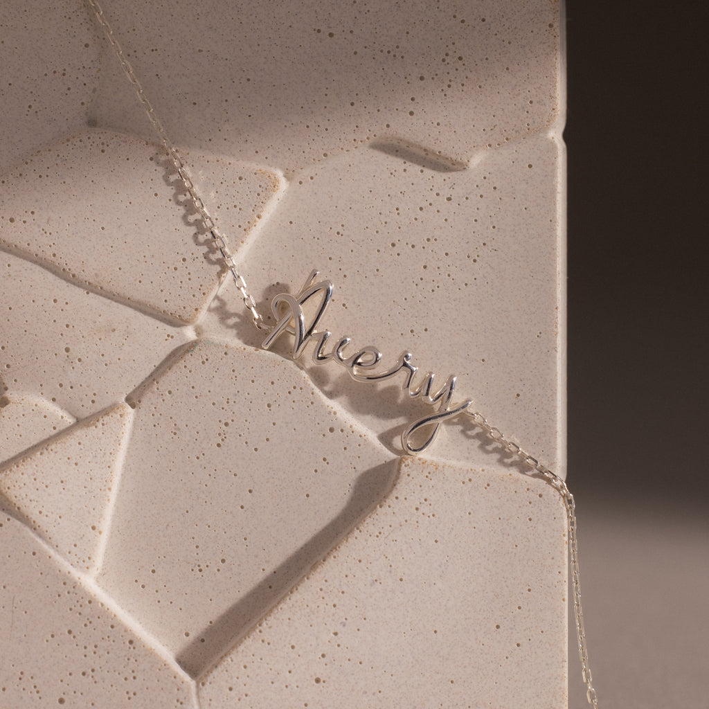 Cursive Name Bracelet in Sterling Silver featuring the name Avery, showcased on a textured beige stone background to highlight the elegance of personalized jewelry.