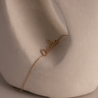 A rose gold cursive name bracelet with "Cecilia" elegantly displayed, draped over a smooth, abstract white sculpture.