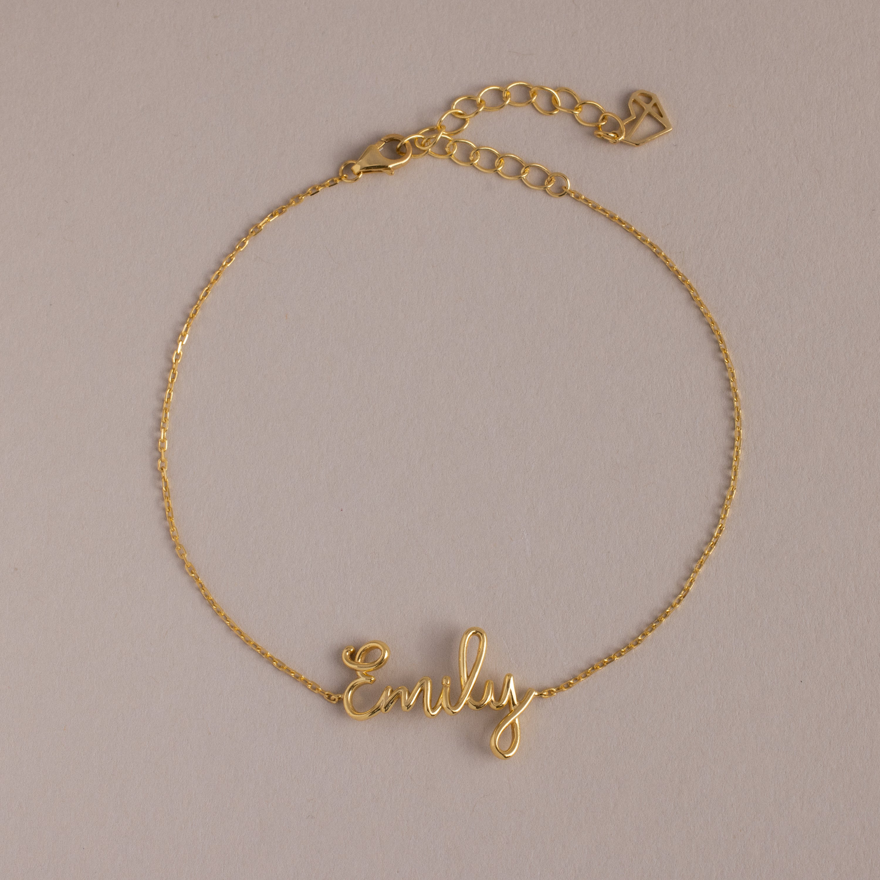 The Cursive Name Bracelet in 18K Gold features "Emily" in elegant script on a neutral background—a perfect personalized gift for custom name jewelry lovers.