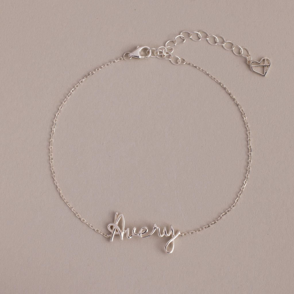 The Cursive Name Bracelet in Sterling Silver features a delicate "Avery" in cursive and a heart charm on an adjustable chain—a perfect, personalized jewelry piece.