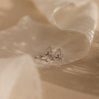 Two delicate Diamond Starburst Drop Studs in Sterling Silver with small diamonds rest on soft, beige, sheer fabric.
