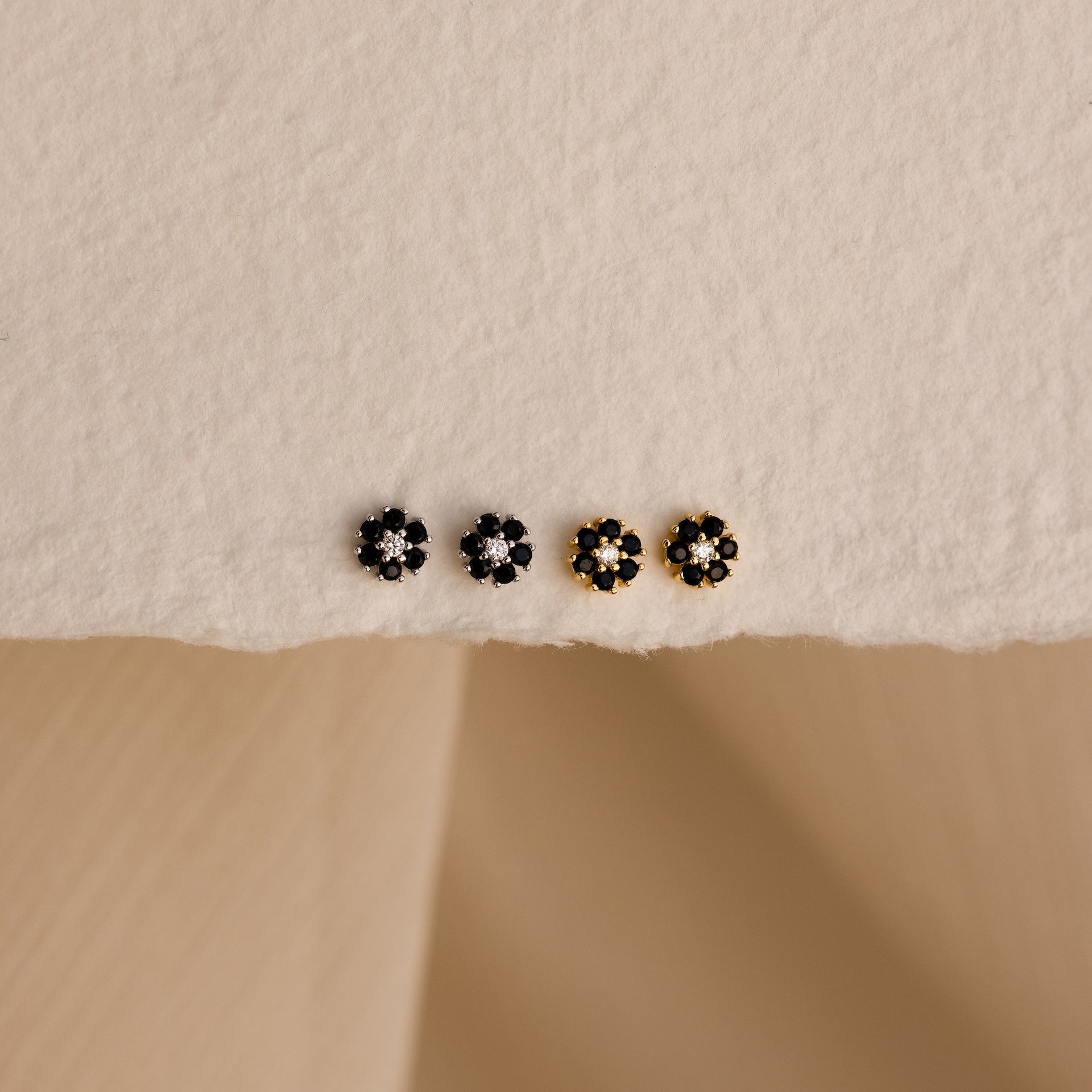 Two silver and two gold small floral stud earrings are arranged on a textured cream surface—style them with Onyx Flower Studs in Silver for a chic, curated ear look.