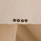 A set of four Onyx Flower Studs—two black onyx and two gold flower-shaped earrings—arranged on a textured cream surface.