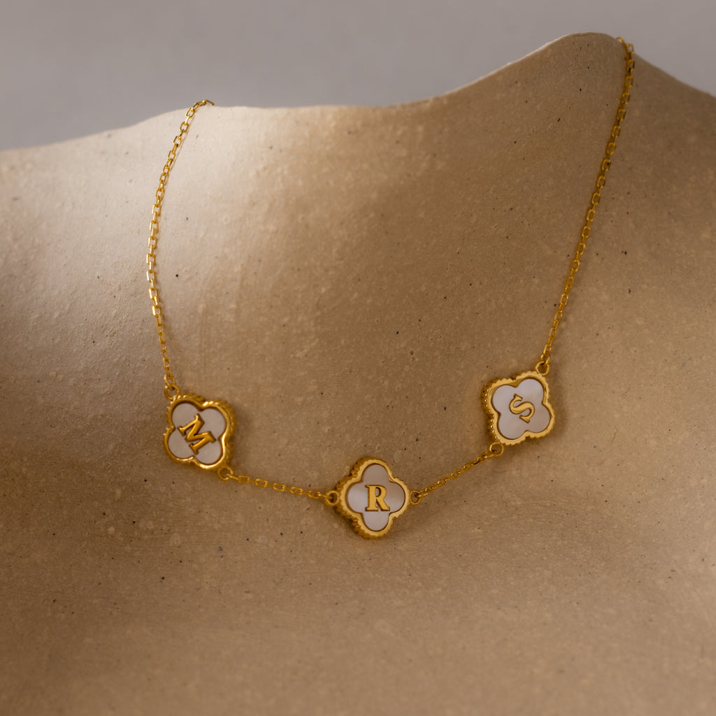 Gold necklace with three clover-shaped charms featuring the letters M, R, and S on a neutral background, reflecting the elegance of the Pearl Clover Letter Bracelet in 18K Gold.