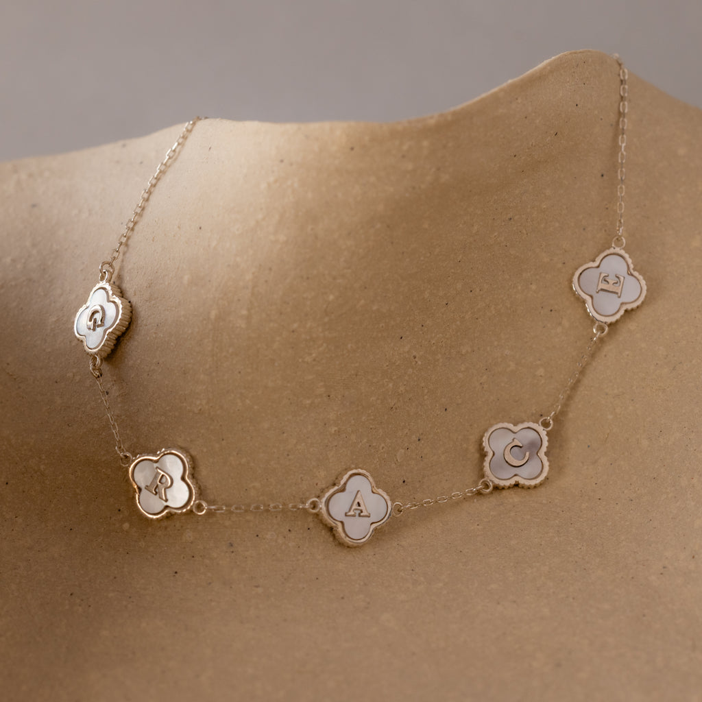 A Pearl Clover Letter Bracelet in Sterling Silver, featuring flower-shaped charms with the letters Q, R, A, C, and R, is showcased on a tan mannequin.