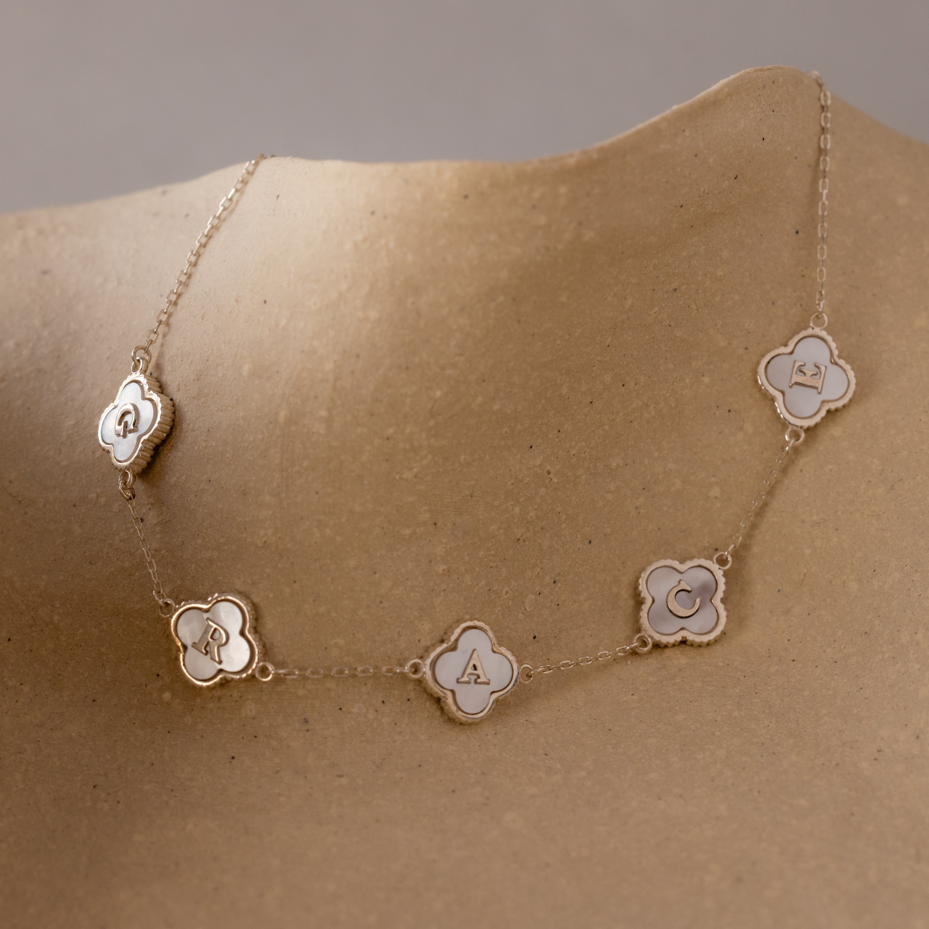 A Pearl Clover Letter Bracelet in Sterling Silver, featuring flower-shaped charms with the letters Q, R, A, C, and R, is showcased on a tan mannequin.