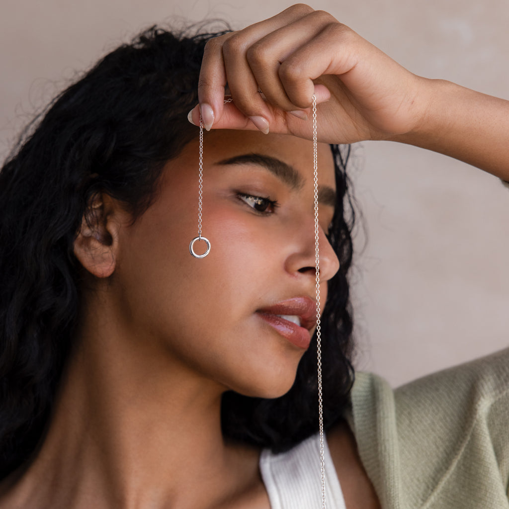A woman holds the Cable Circle Charm Necklace in Sterling Silver with a circular pendant near her face, gazing to the side.