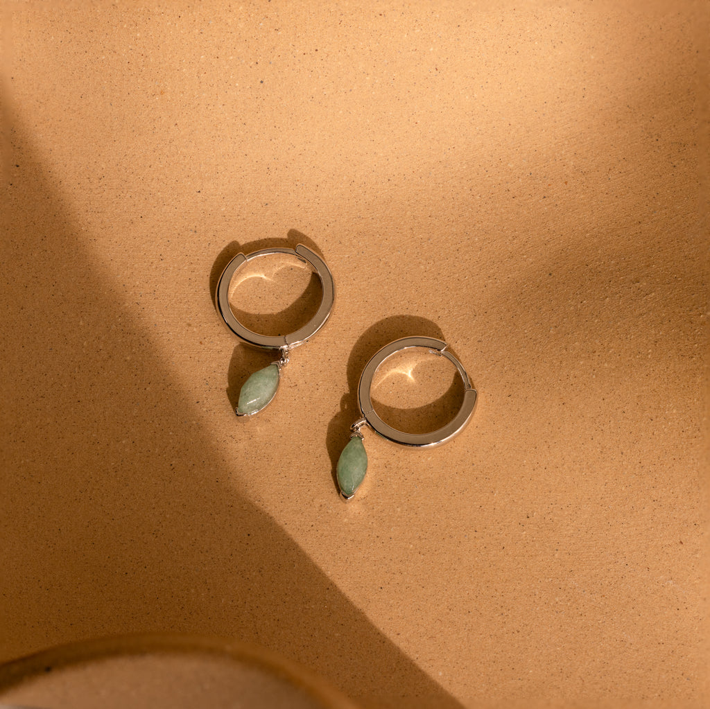 Jade Marquise Huggies in Silver displayed on a sandy beige background under soft light.