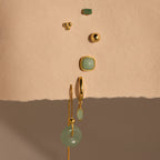 Jade Marquise Huggies in 18K Gold, along with green gemstone jewelry, arranged vertically on a textured beige surface.