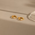 The Rhombus Opal Huggies are gold hoop earrings featuring diamond-shaped white opal inlays, offering a modern twist on classic gemstone hoops, elegantly presented on a beige surface with gentle shadows.