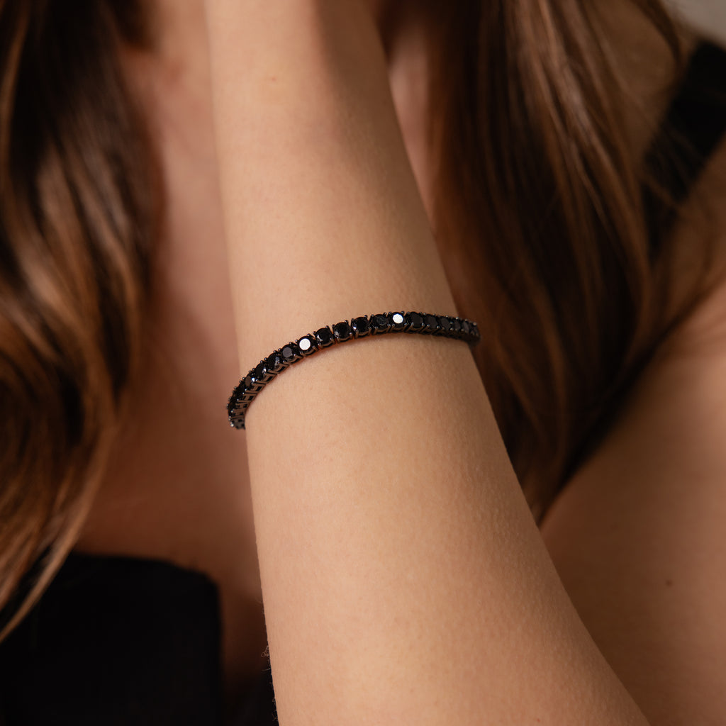 A woman with long brown hair and a black top wears the Onyx Tennis Bracelet on her wrist.
