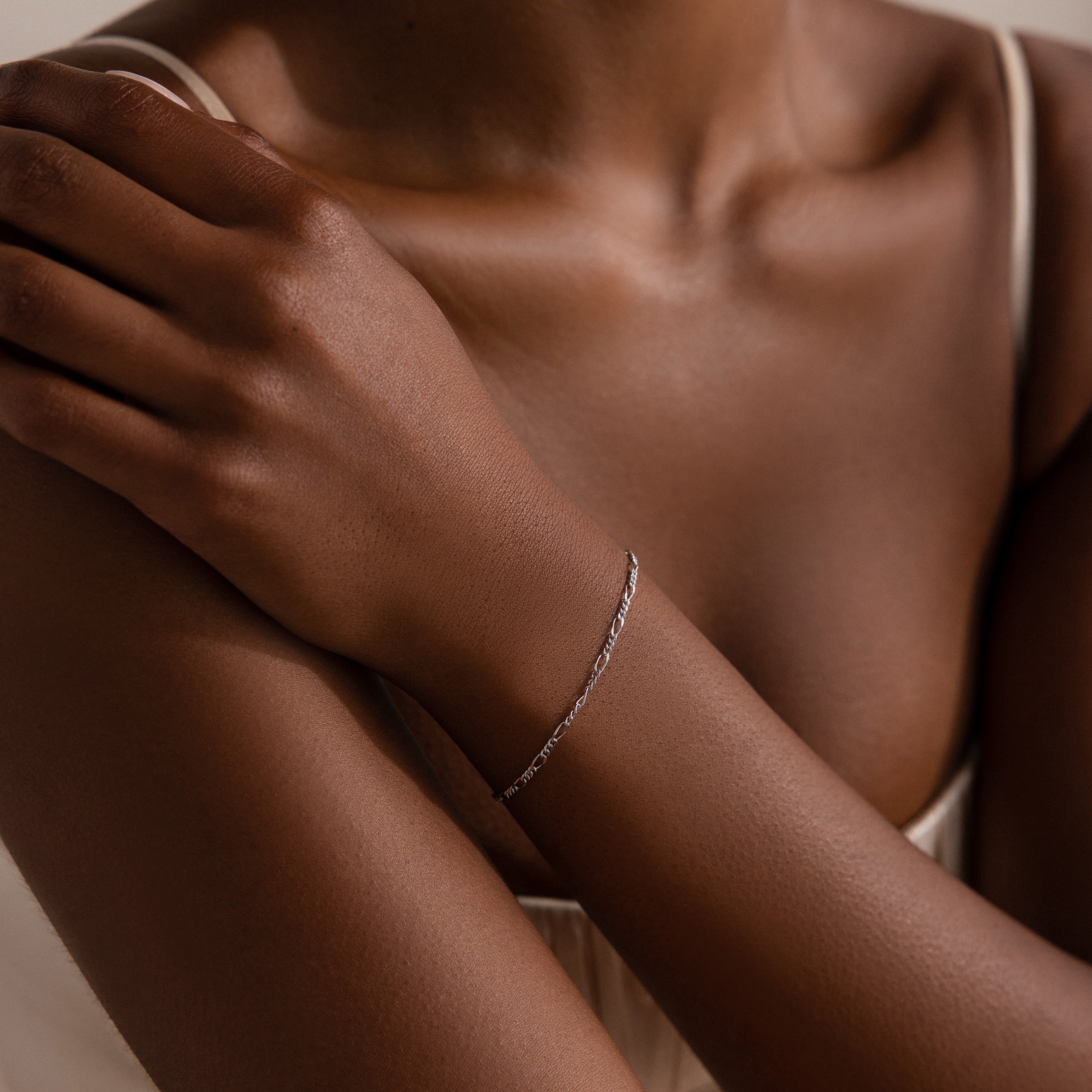 Close-up of a person's arm with a silver chain bracelet on a neutral background