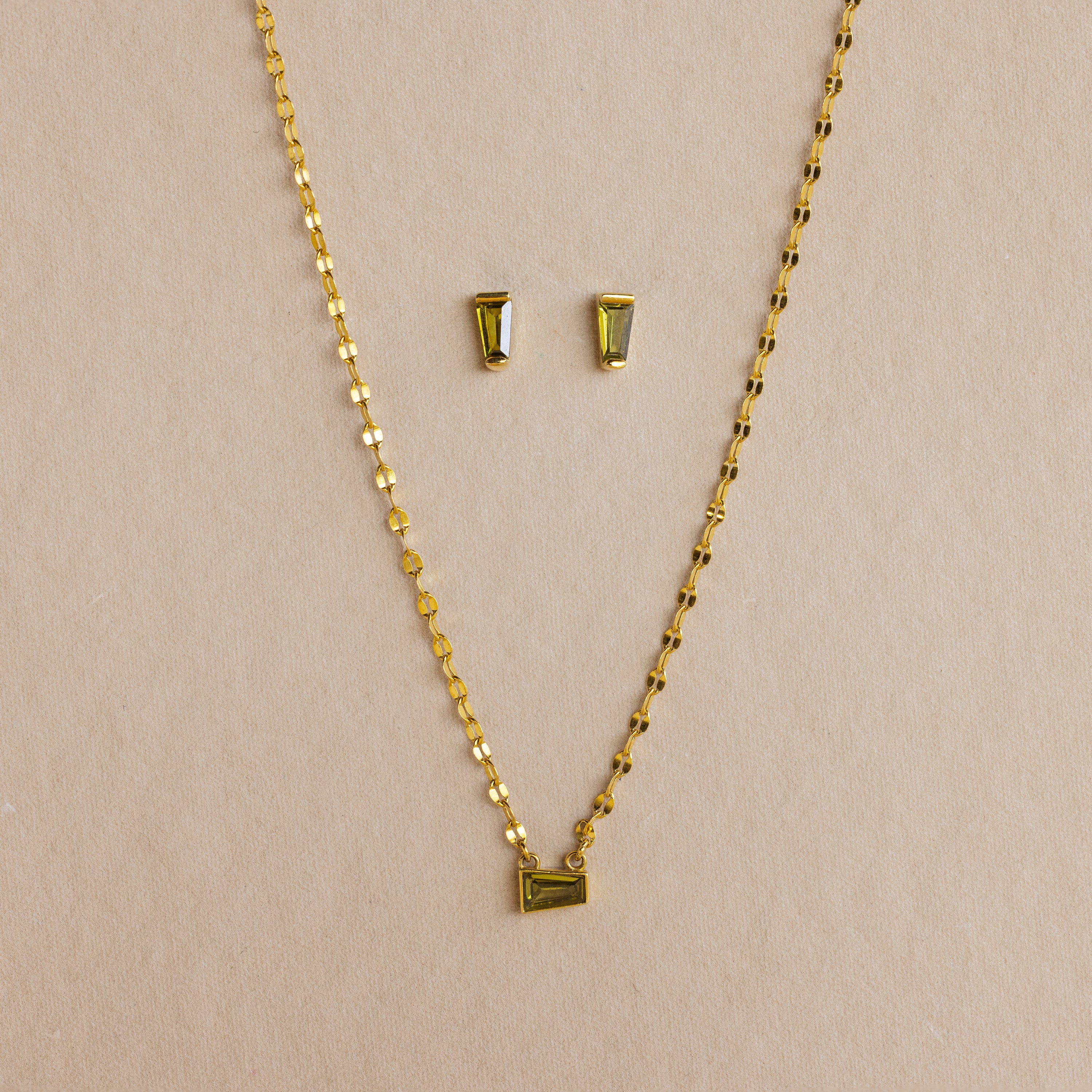 Tapered Baguette Birthstone Studs and a gold chain necklace with a rectangular pendant are displayed together against a neutral background.