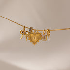 Multiple gold charms hang side by side on a gold dainty curb chain, including the gold ribbed vintage heart charm, an initial charm, heart moonstome charm, diamond infinity charm and bow charm 