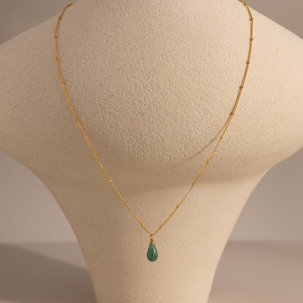 Minimal gold satellite chain necklace featuring a single green jade teardrop gemstone pendant, displayed on a neutral stand.