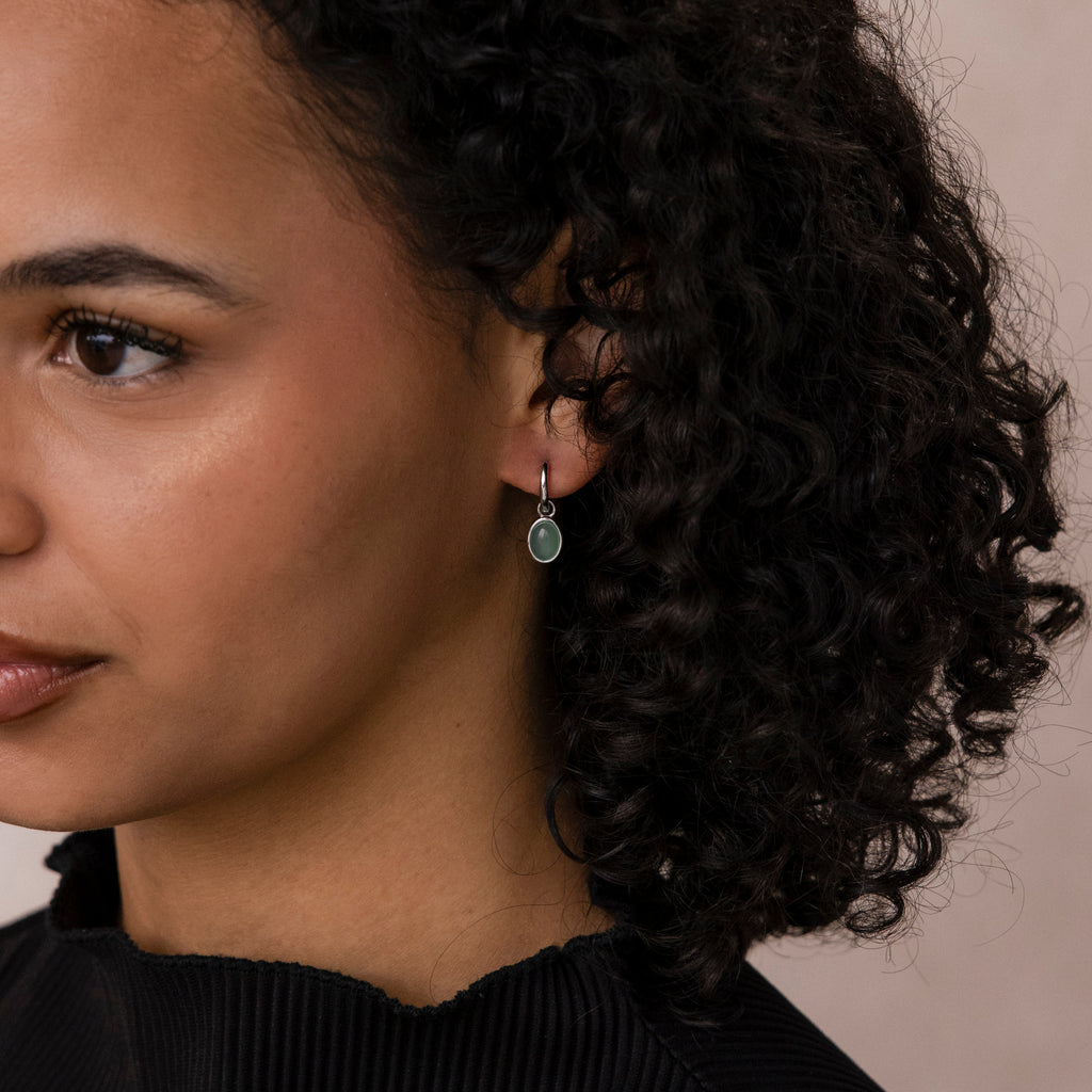 Close-up of a woman with curly hair wearing Jade Drop Hoops earrings and a black top.