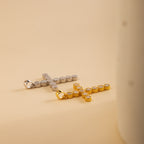 A gold and a silver pave cross charm lay flatly, side by side