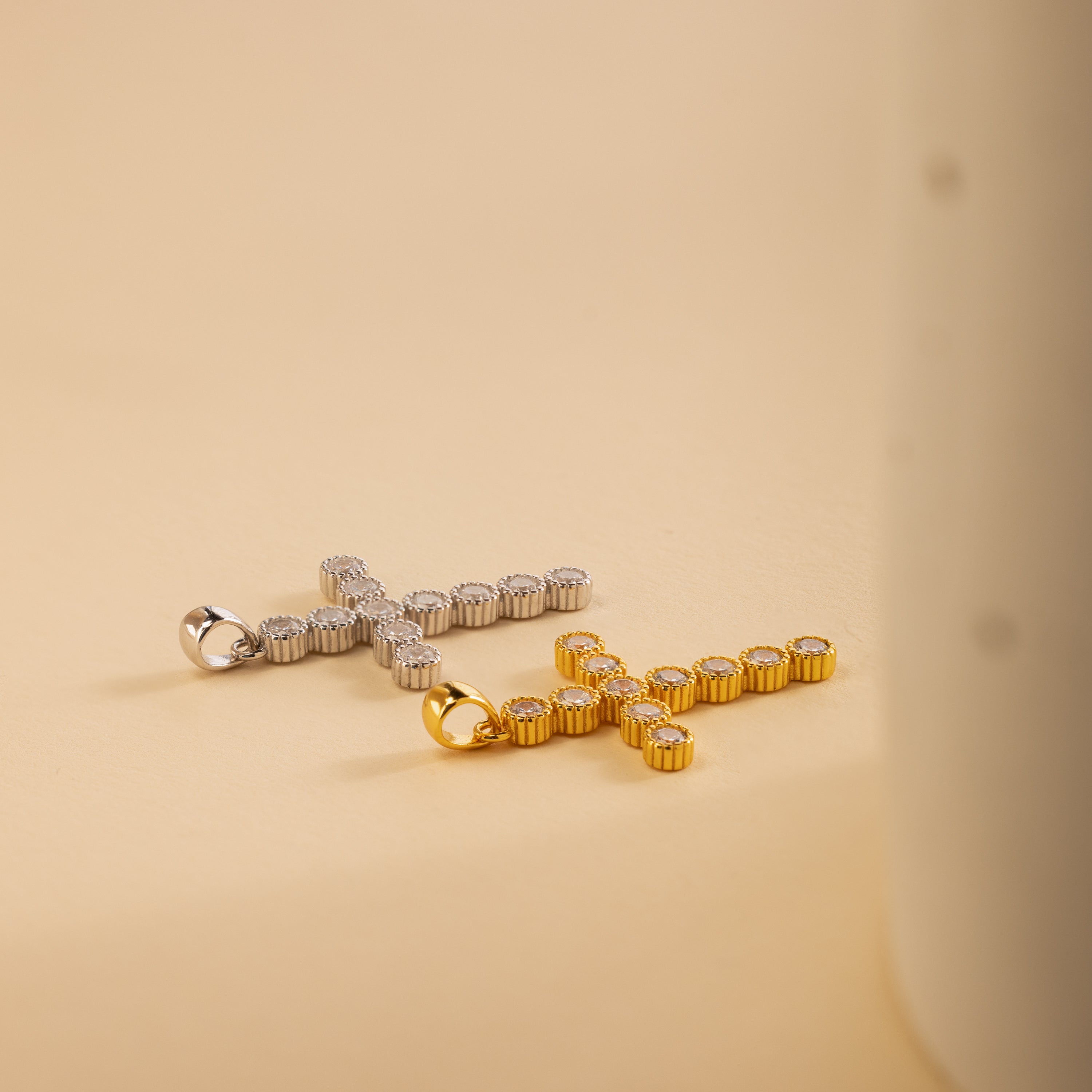 A gold and a silver pave cross charm lay flatly, side by side