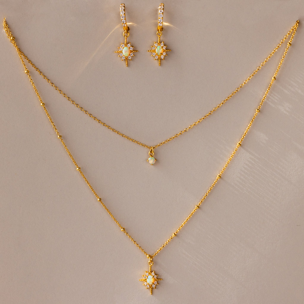 The Opal Star Necklace & Earrings Set includes a gold-layered necklace with opal star pendants and matching star-shaped earrings, beautifully displayed on a beige surface.