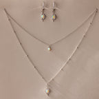The Opal Star Necklace & Earrings Set in Silver features shimmering opal and crystal starburst pendants, beautifully displayed on a beige background.