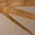 The Opal Star Necklace & Earrings Set in 18K Gold features sunburst designs, elegantly displayed on dried palm leaves against a beige background.