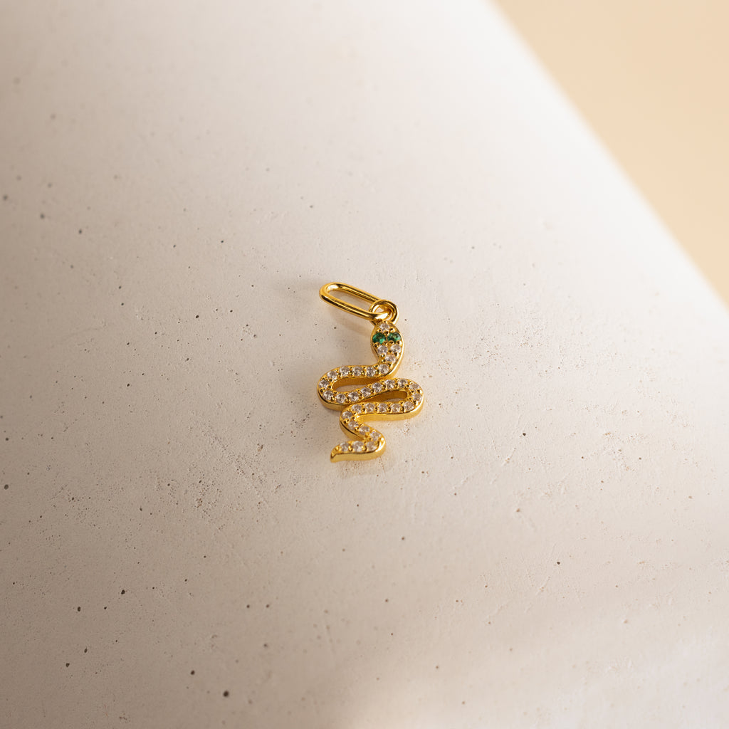 A gold diamond snake charm. The design is a twisting snake with diamond gemstones encased on its body and emerald gemstones for its eyes