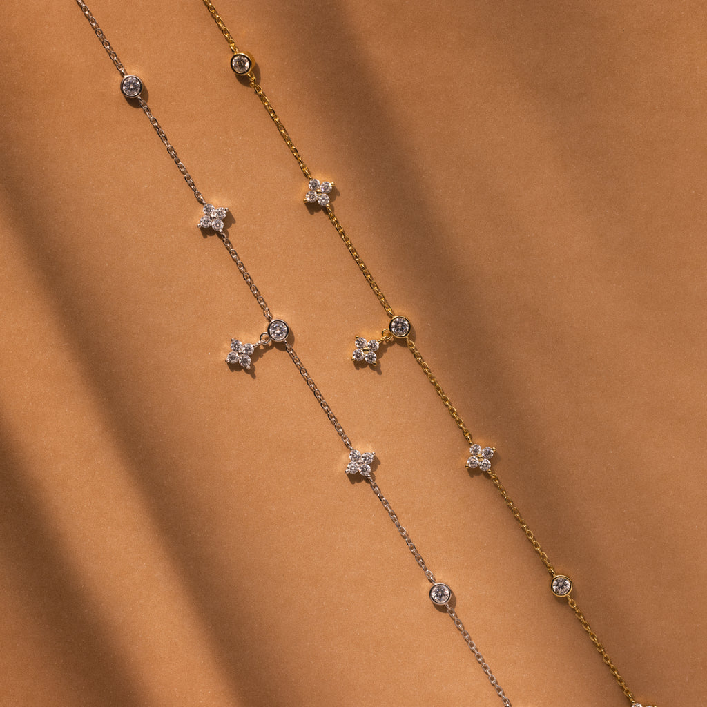 The Ivy Diamond Station Necklace features delicate diamond accents on a silver and gold chain with star and round charms, displayed on a brown background.