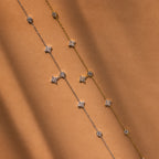 The Ivy Diamond Station Necklace features delicate diamond accents on a silver and gold chain with star and round charms, displayed on a brown background.