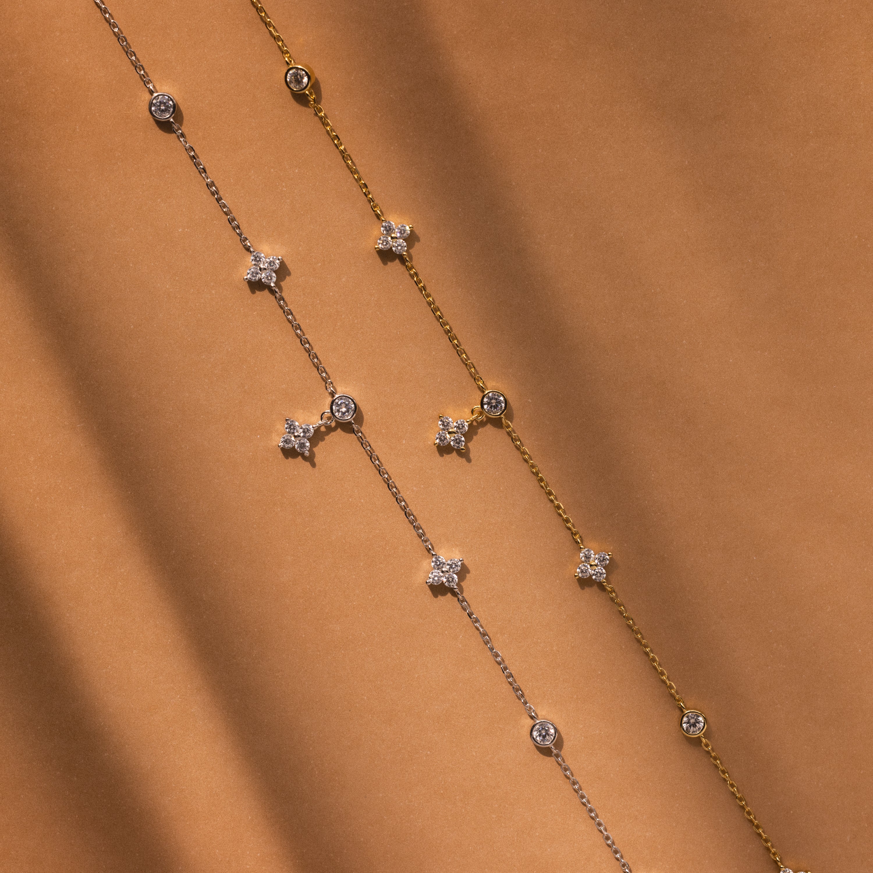 The Ivy Diamond Station Necklace features delicate diamond accents on a silver and gold chain with star and round charms, displayed on a brown background.