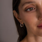 A close-up of a woman wearing Beaded Hoops in Sterling Silver—silver earrings adorned with small pearl-like beads that catch the light for a textured glow.
