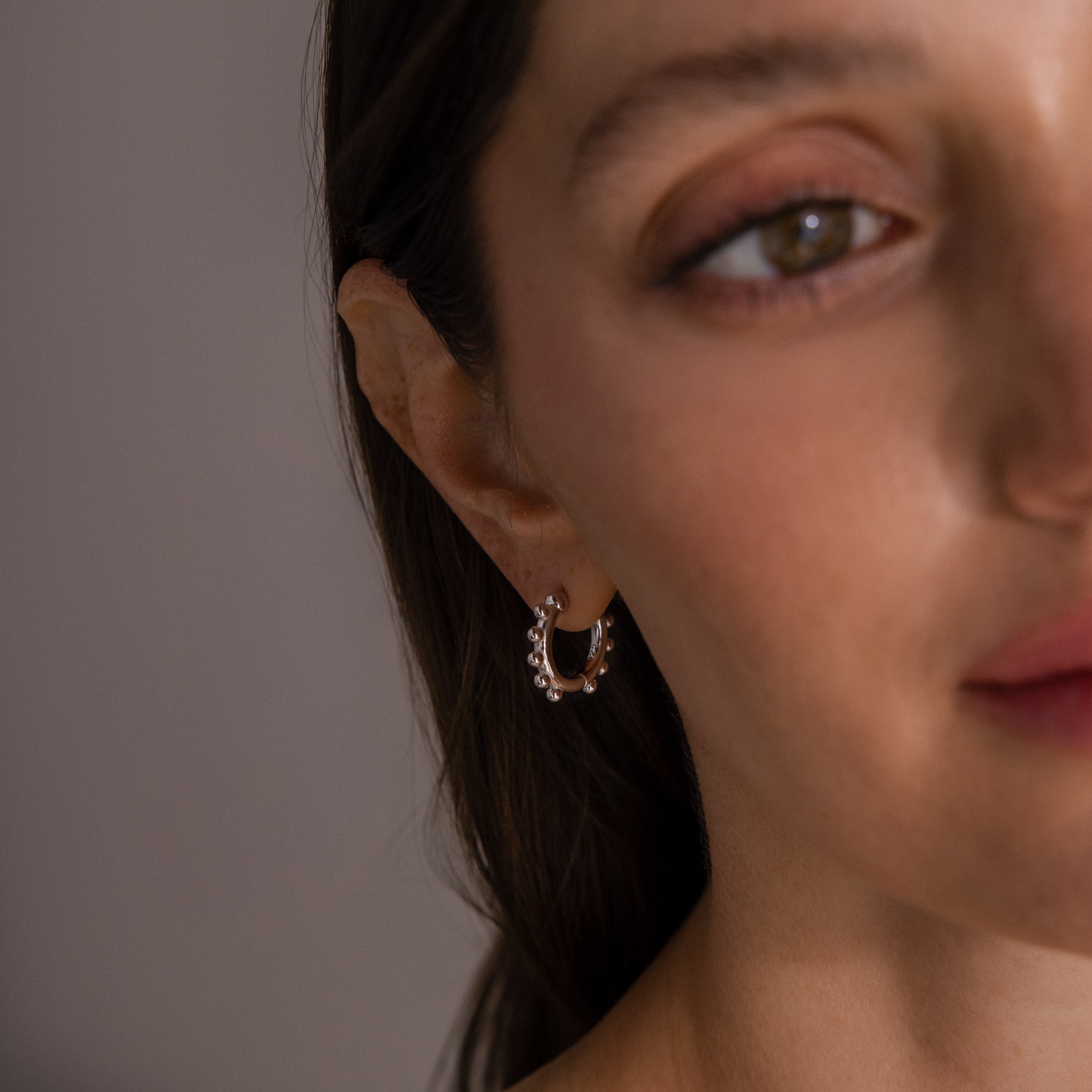 A close-up of a woman wearing Beaded Hoops in Sterling Silver—silver earrings adorned with small pearl-like beads that catch the light for a textured glow.