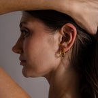 A woman with brown hair models the Beaded Hoops—gold earrings with polished beads and an ear cuff—her arm raised behind her head, set against a neutral background.