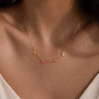 The Dainty Space Charm Necklace features gold letter charms H and C, plus a pink heart charm, worn with a white top—an ideal customizable necklace for any occasion.