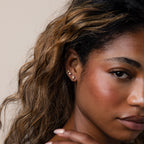 Close-up of a woman with wavy hair wearing Halo Moonstone Drop Studs and gold earrings, looking at the camera.
