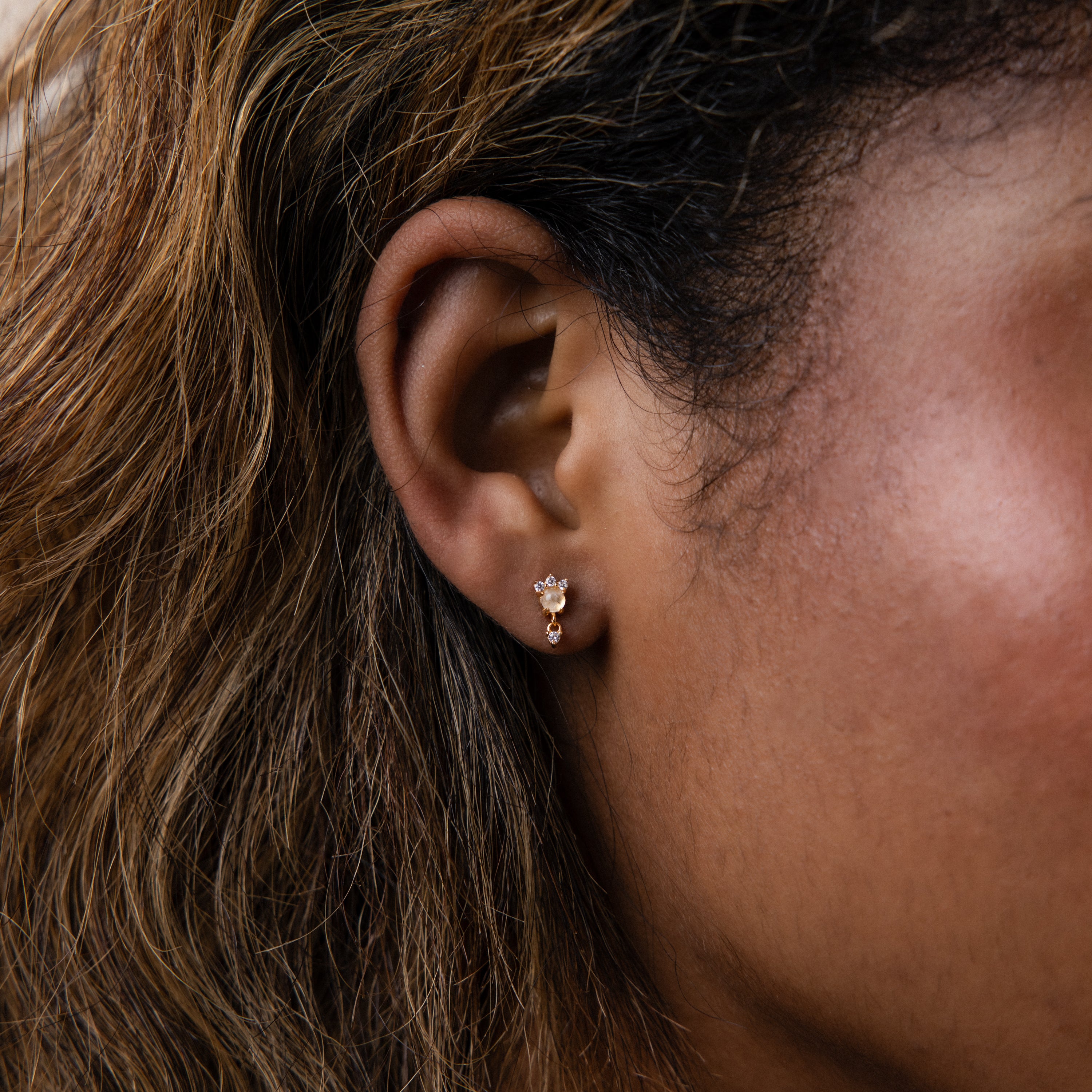 Close-up of a woman's ear adorned with Halo Moonstone Drop Studs, highlighted by light brown wavy hair.