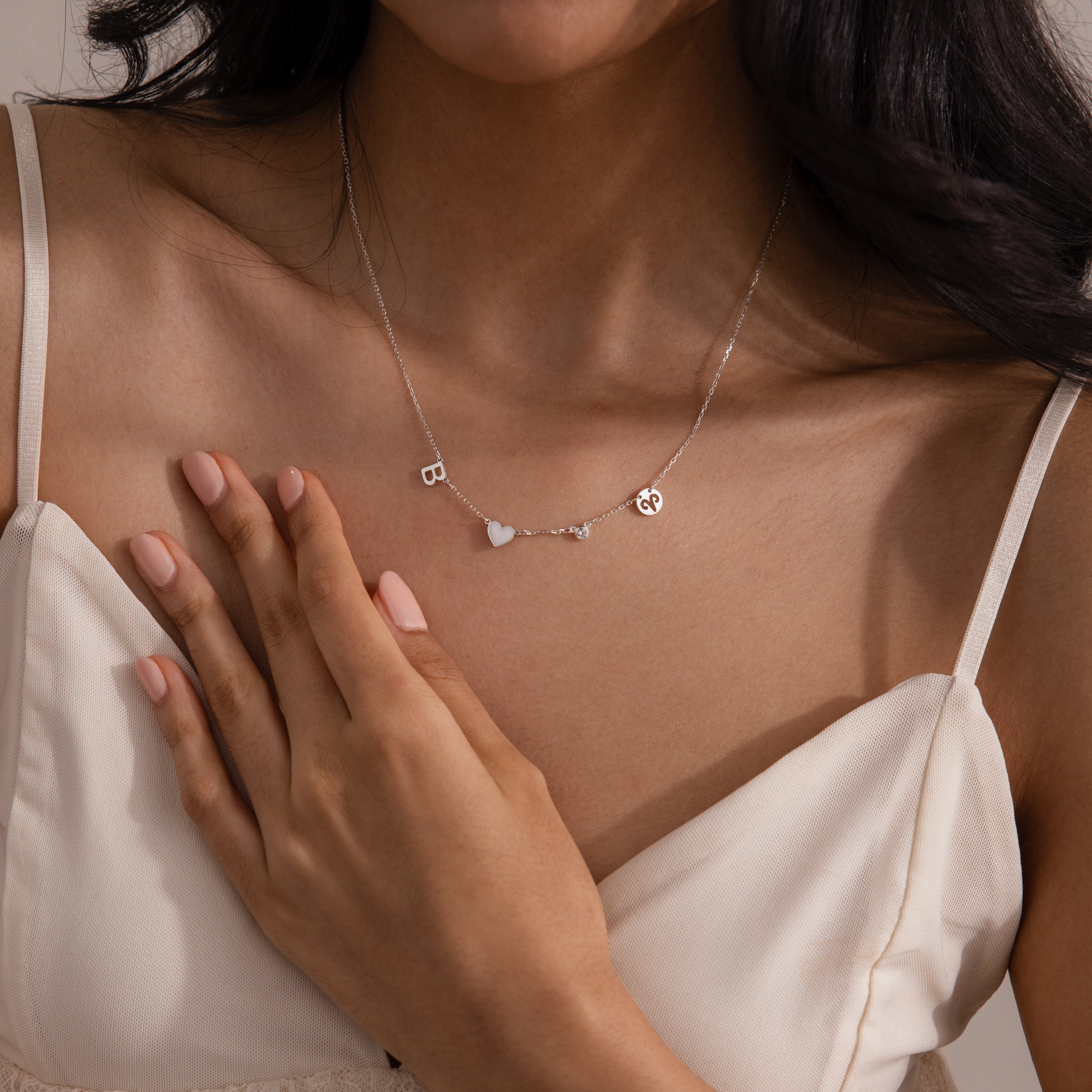 A woman in a cream dress wears the Dainty Space Charm Necklace, her hand resting gently on her chest.