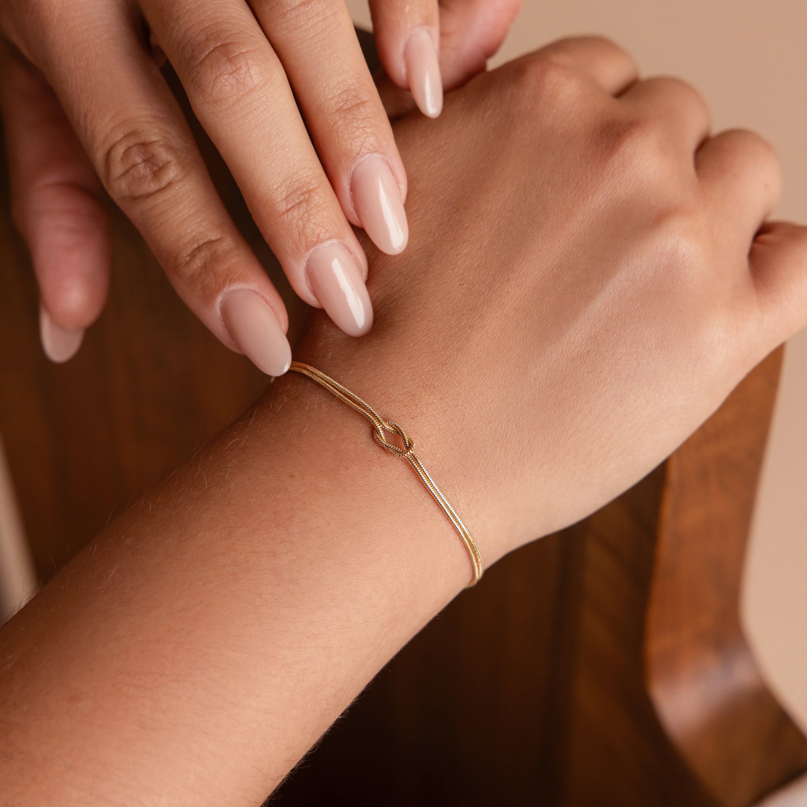 A hand with nude nails wears the Love Knot Bracelet—a delicate double chain that gently touches the wrist, making it a perfect gift for couples.