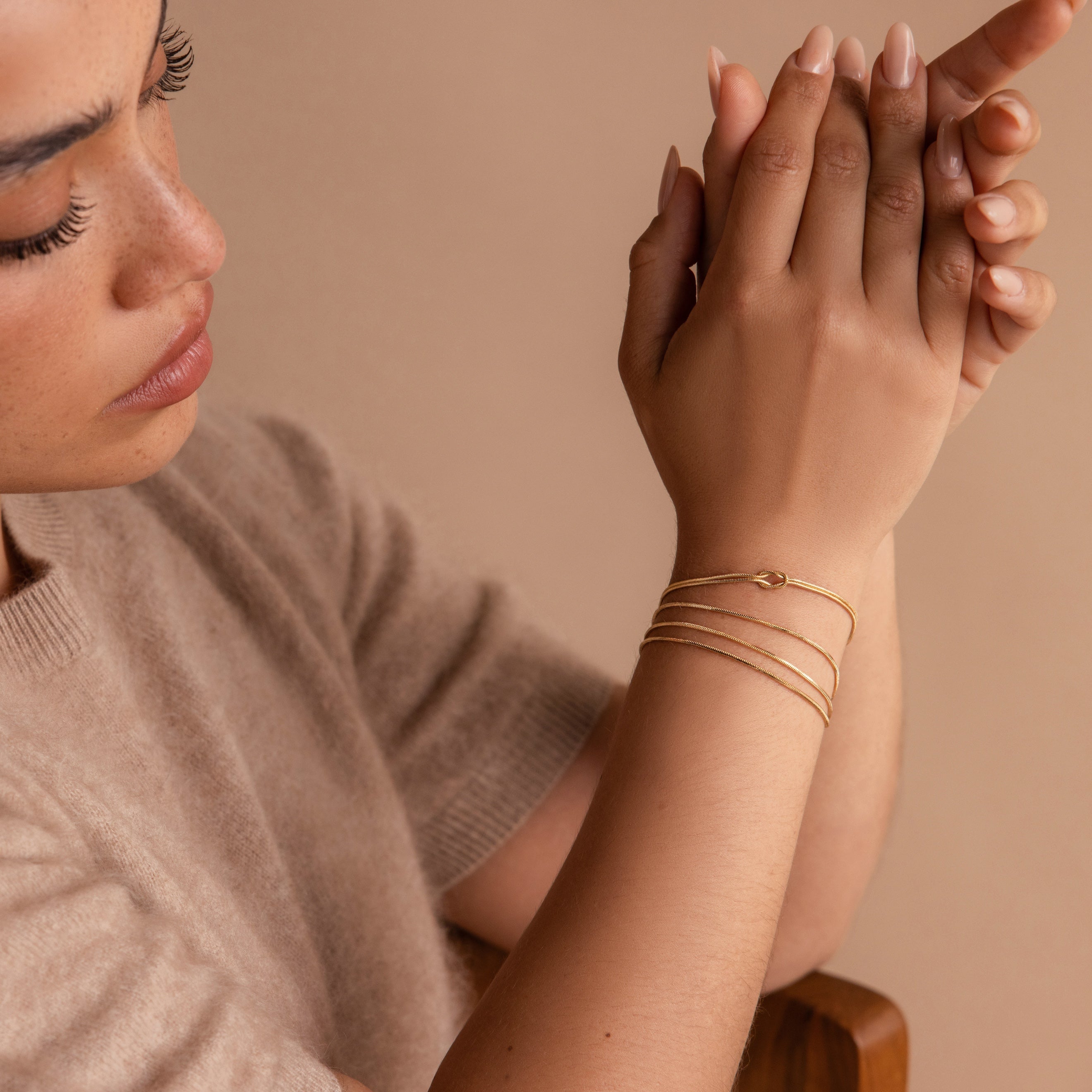 A woman in a beige sweater clasps her hands, highlighting the Love Knot Bracelet—a perfect, elegant gift for couples—against a neutral background.