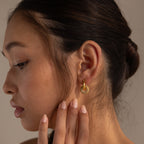 A woman with a low bun touches her neck, wearing Duo Pave Link Hoops in 18K Gold featuring a bold, textured design.
