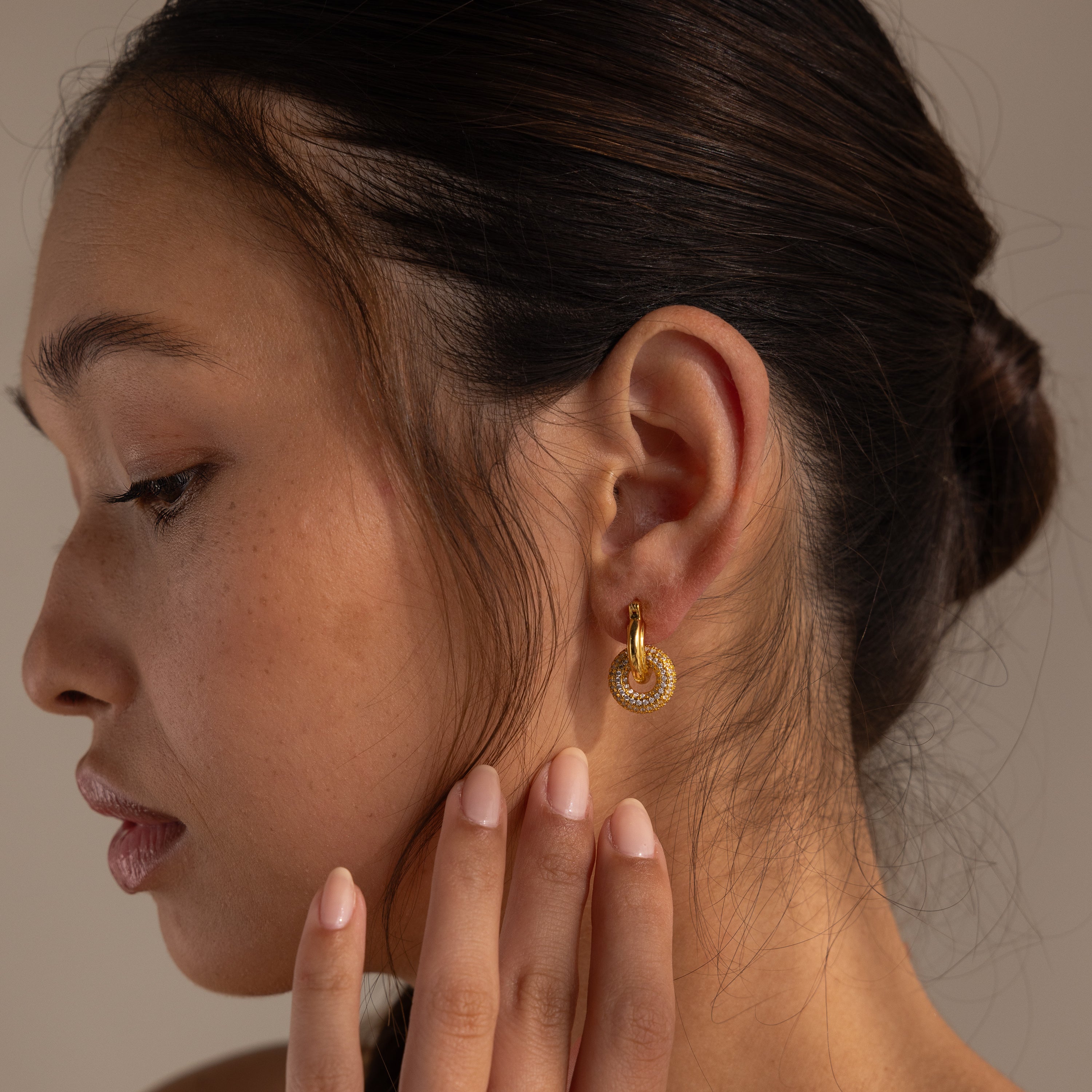 A woman with a low bun touches her neck, wearing Duo Pave Link Hoops in 18K Gold featuring a bold, textured design.