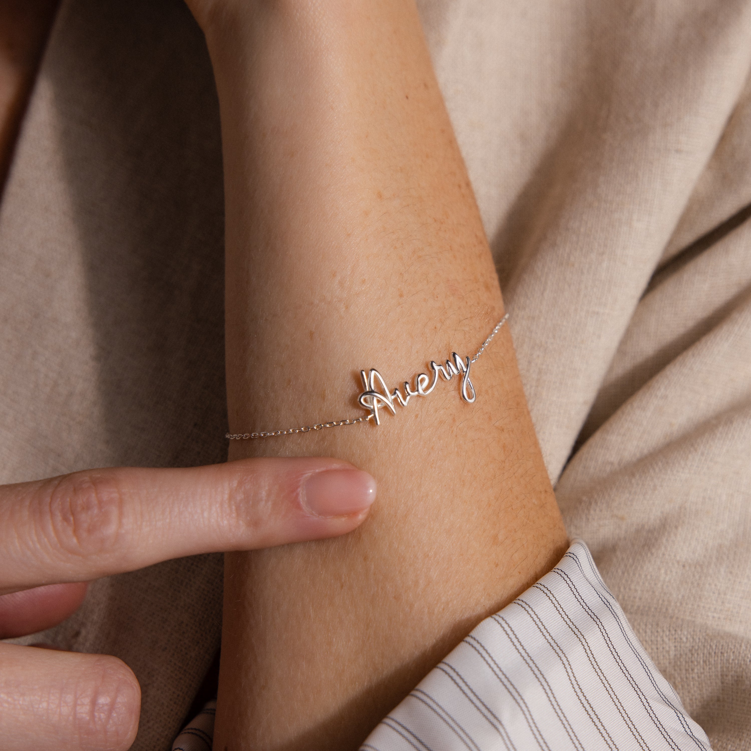 A hand showcases the Cursive Name Bracelet in Sterling Silver on a wrist, featuring the name Avery—a striking example of custom jewelry.