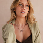 Woman with wavy blonde hair wears a Bar & Carabiner Charm Set in White Gold and a light green cardigan, looking upward.