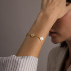 Close-up of a woman’s wrist wearing the Pearl Clover Letter Bracelet in Rose Gold, featuring white mother of pearl floral charms, with her hand near her face.