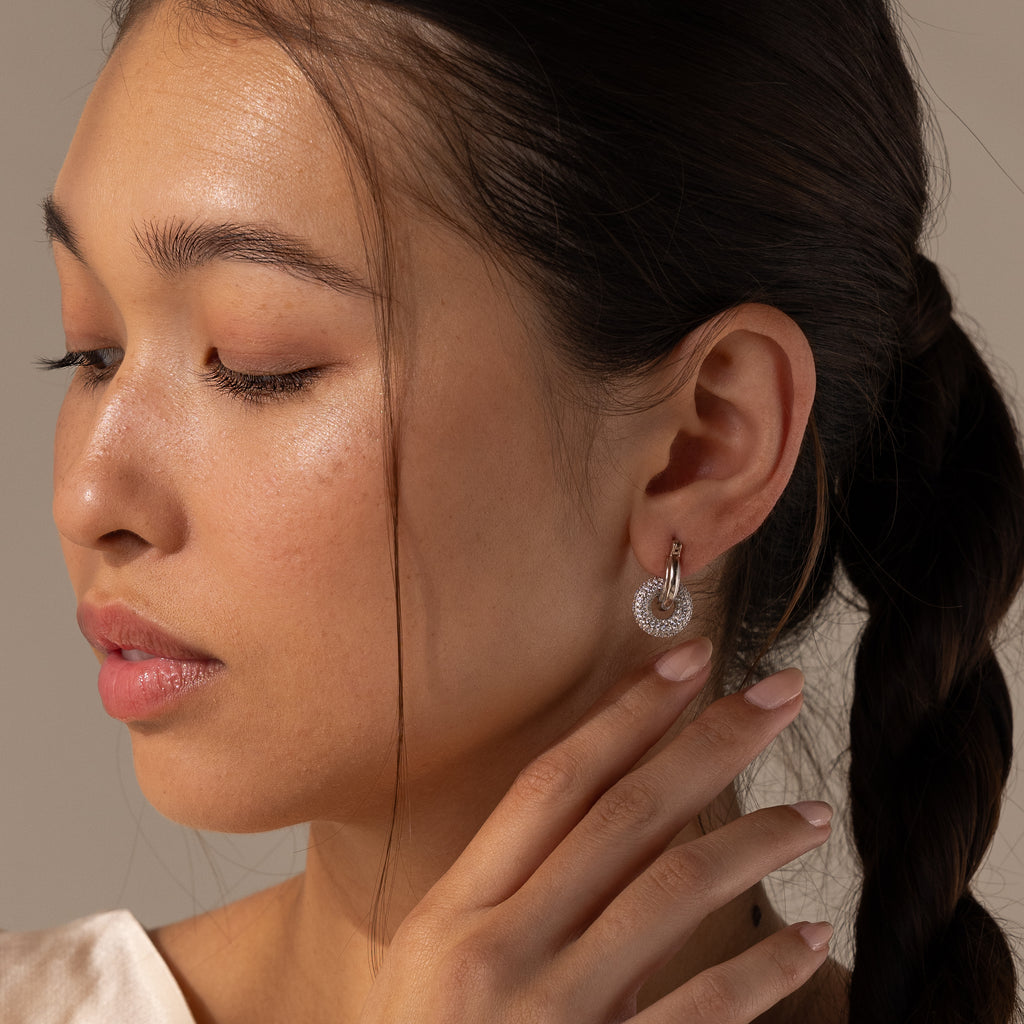 Woman with braided hair wears Duo Pave Link Hoops in White Gold, gently touching her ear and gazing downward with a soft expression.