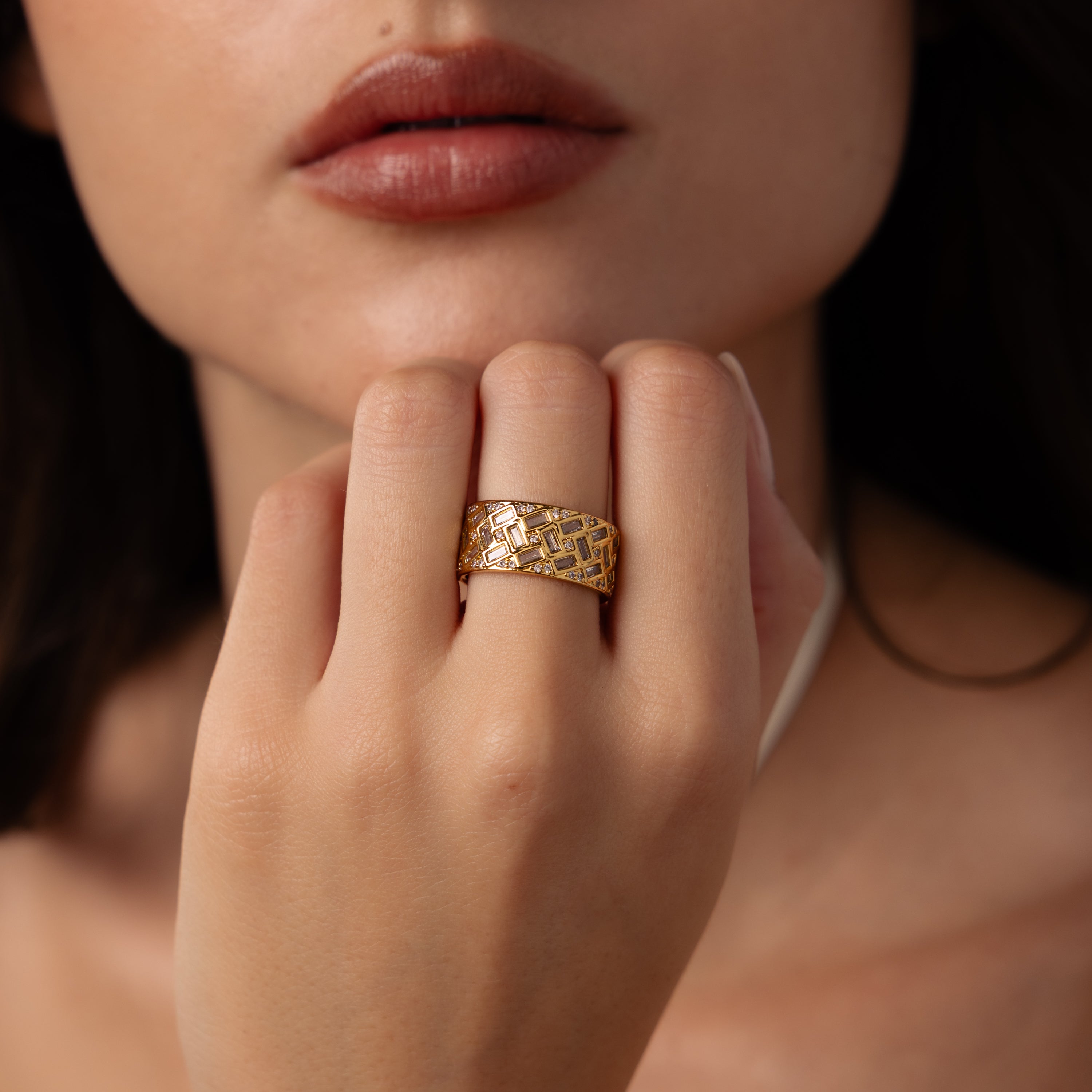 A woman’s hand with the Mosaic Diamond Baguette Ring, its bold pattern gleaming, rests near her lips.