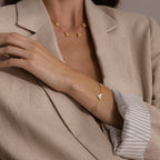 Woman in a beige blazer wears a gold necklace and the Pearl Clover Letter Bracelet in Rose Gold, featuring floral-shaped charms.