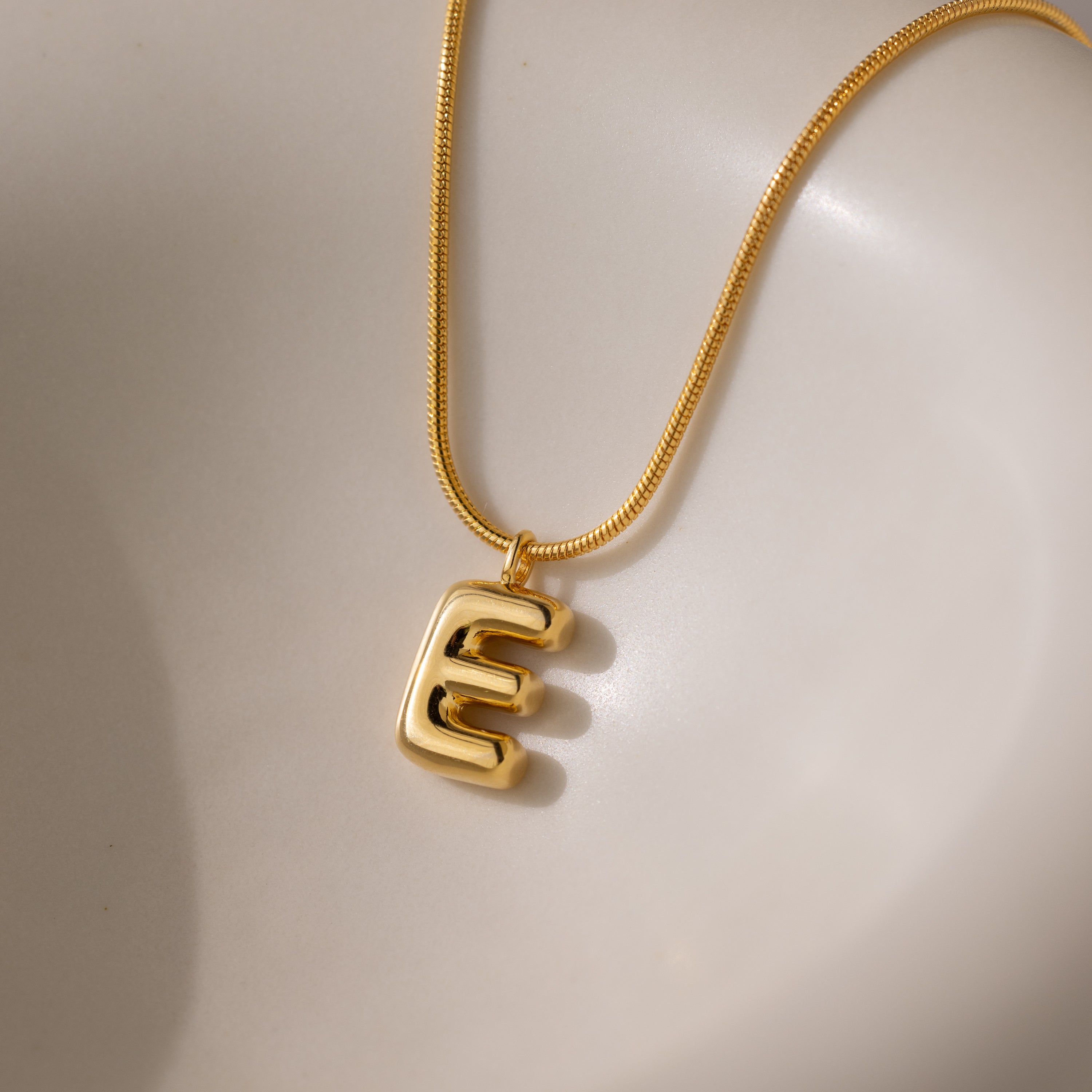 The Bubble Letter Necklace in 18K Gold features a shiny bubble letter E pendant on a smooth, light background—ideal for anyone who loves personalized jewelry.