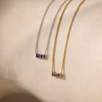 Two Emery Birthstone Necklaces with rectangular amethyst gemstones, one set in gold and the other in silver, displayed side by side.